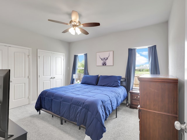 carpeted bedroom featuring ceiling fan and multiple closets