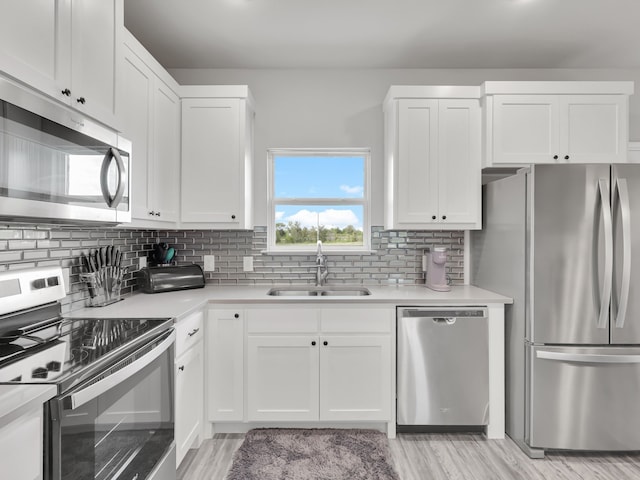 kitchen with stainless steel appliances, sink, white cabinetry, and light hardwood / wood-style floors