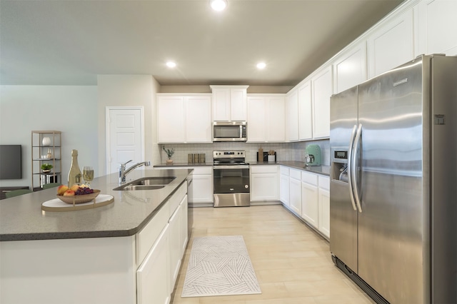 kitchen with tasteful backsplash, stainless steel appliances, an island with sink, sink, and white cabinets