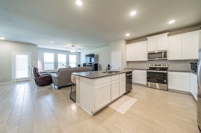 kitchen with sink, ceiling fan, appliances with stainless steel finishes, a center island with sink, and white cabinets