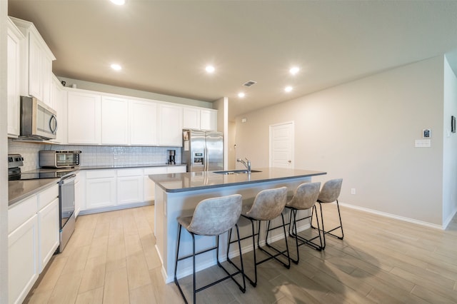 kitchen featuring light hardwood / wood-style flooring, a kitchen island with sink, stainless steel appliances, sink, and white cabinetry