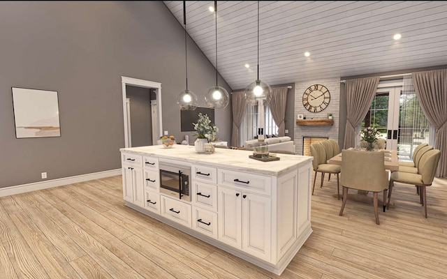 kitchen with high vaulted ceiling, a brick fireplace, hanging light fixtures, stainless steel microwave, and white cabinets