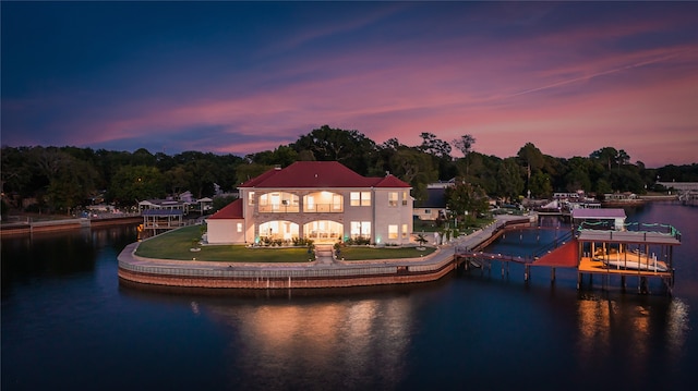 back house at dusk featuring a lawn and a water view