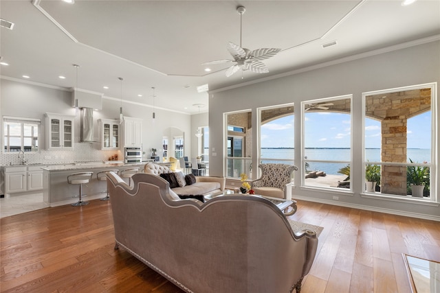 living room with a water view, ceiling fan, hardwood / wood-style flooring, and ornamental molding