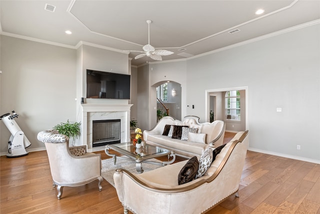 living room featuring crown molding, light hardwood / wood-style flooring, ceiling fan, and a high end fireplace