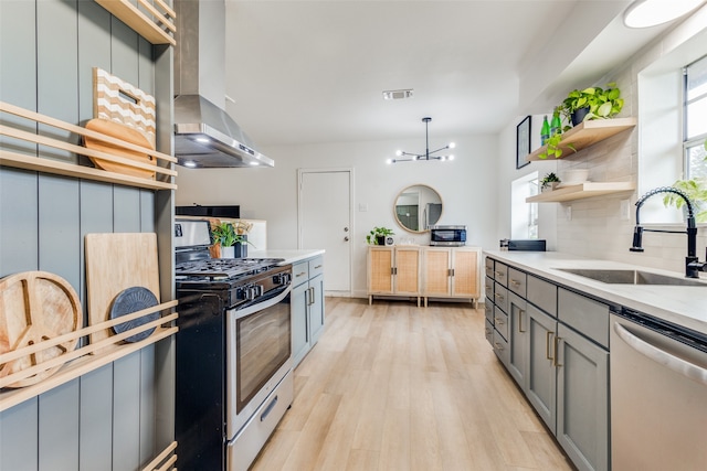 kitchen featuring gray cabinetry, appliances with stainless steel finishes, light hardwood / wood-style floors, sink, and wall chimney range hood