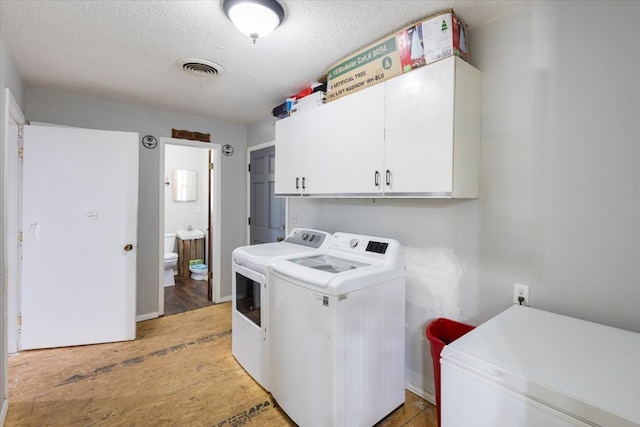 laundry room with wood-type flooring, washer and dryer, cabinets, and a textured ceiling