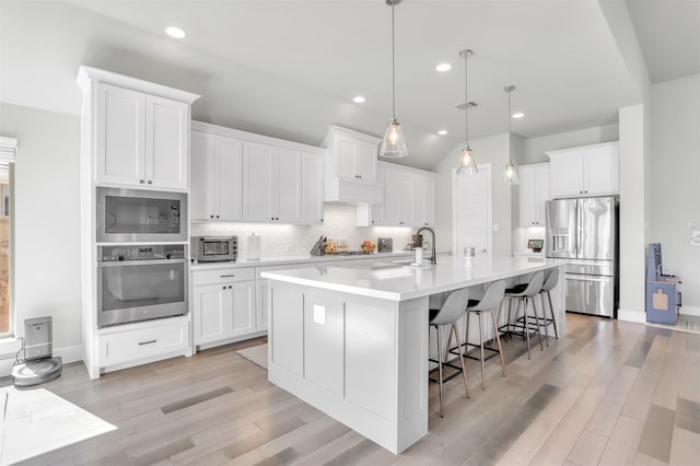 kitchen with decorative light fixtures, white cabinets, a kitchen island with sink, a breakfast bar, and appliances with stainless steel finishes