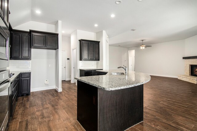 kitchen with decorative backsplash, a fireplace, dark hardwood / wood-style floors, lofted ceiling, and an island with sink