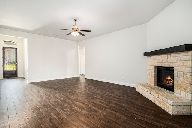 unfurnished living room with a stone fireplace, ceiling fan, and dark hardwood / wood-style flooring