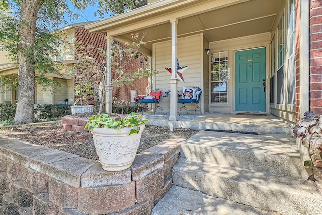 doorway to property featuring covered porch and brick siding