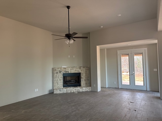 unfurnished living room with ceiling fan, a stone fireplace, and wood-type flooring