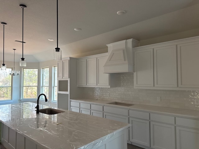 kitchen featuring pendant lighting, premium range hood, a kitchen island with sink, and sink