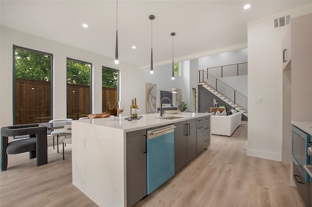 kitchen featuring decorative light fixtures, dishwasher, light hardwood / wood-style floors, an island with sink, and sink