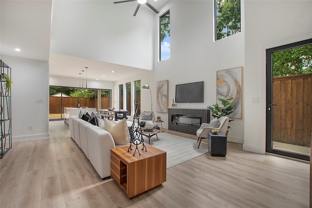 living room with light wood-type flooring, ceiling fan, and a high ceiling