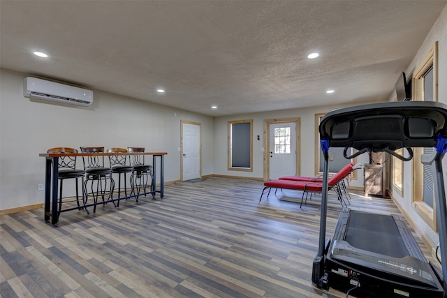 exercise area featuring a textured ceiling, wood-type flooring, and a wall mounted air conditioner