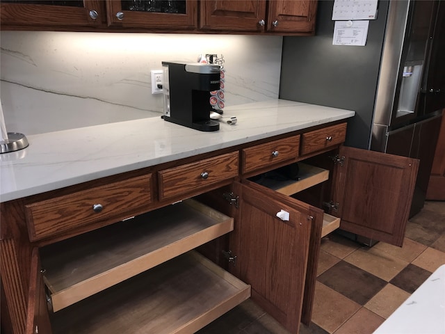 kitchen with light stone countertops, dark brown cabinetry, and stainless steel refrigerator with ice dispenser