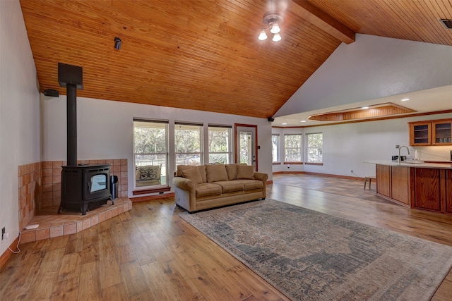 living room featuring a wood stove, high vaulted ceiling, sink, and light wood-type flooring