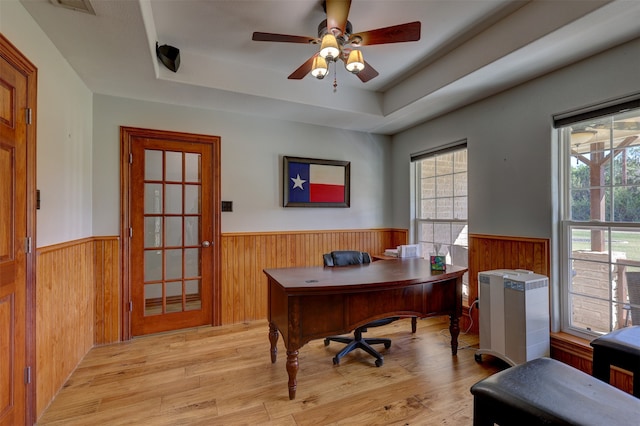 office space with a tray ceiling, ceiling fan, light hardwood / wood-style floors, and wood walls