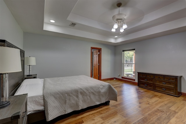 bedroom with light wood-type flooring, a tray ceiling, and ceiling fan