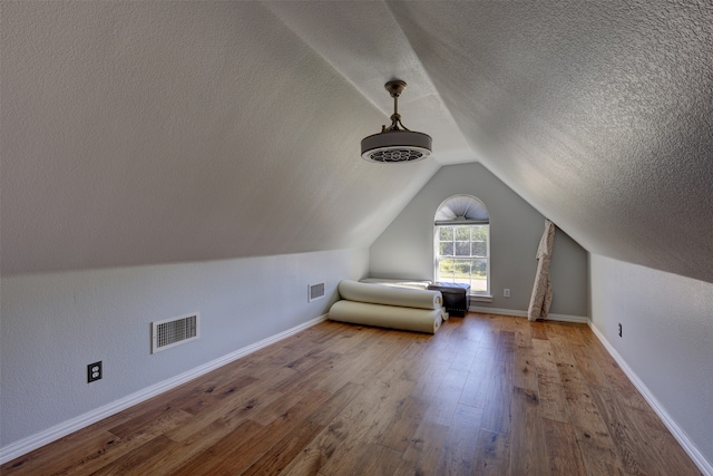 additional living space featuring lofted ceiling, wood-type flooring, and a textured ceiling