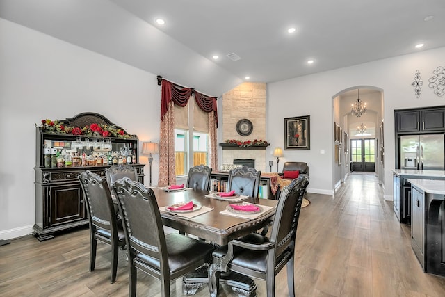 dining room with a notable chandelier, lofted ceiling, a stone fireplace, and light wood-type flooring