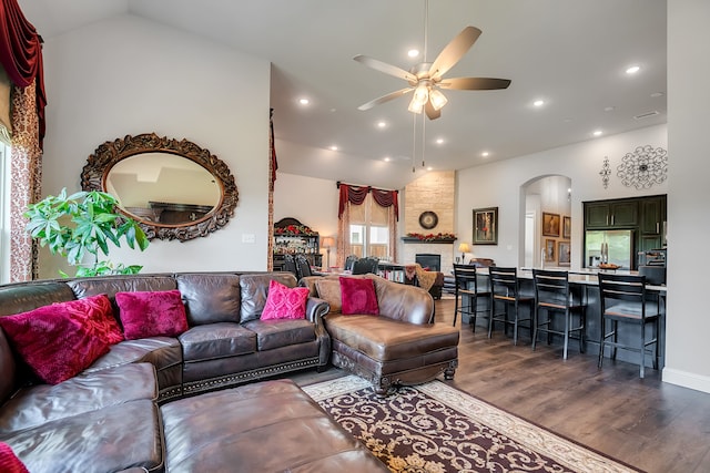 living room featuring high vaulted ceiling, a large fireplace, dark wood-type flooring, and ceiling fan