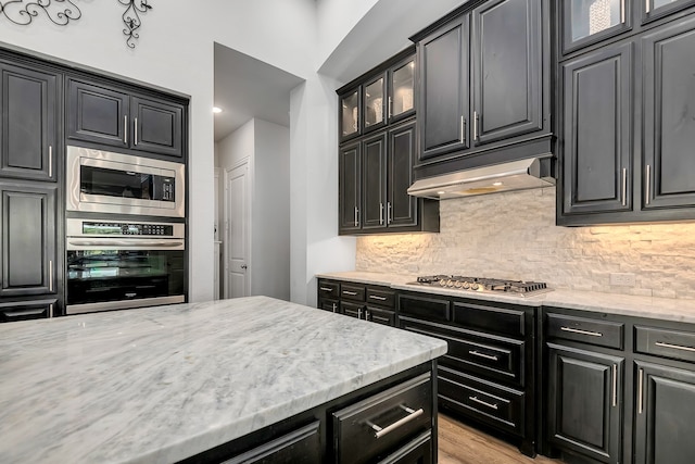 kitchen with tasteful backsplash, ventilation hood, light hardwood / wood-style floors, stainless steel appliances, and light stone countertops