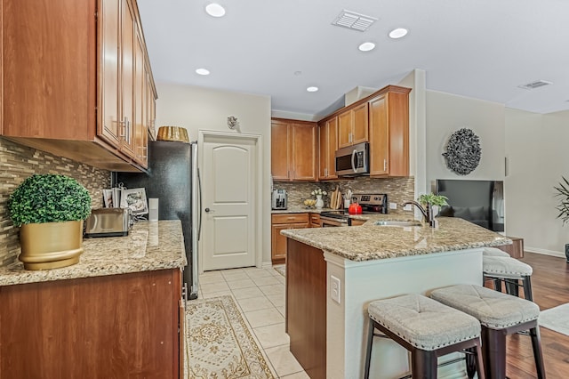 kitchen with a kitchen bar, kitchen peninsula, sink, light stone countertops, and appliances with stainless steel finishes