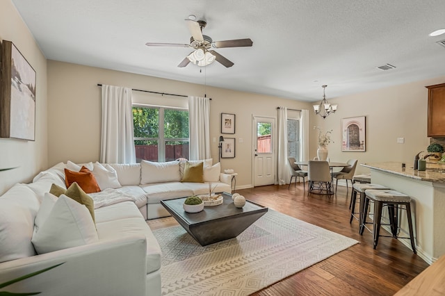 living room featuring ceiling fan with notable chandelier, dark hardwood / wood-style floors, and a textured ceiling