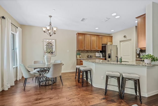 kitchen featuring dark hardwood / wood-style floors, light stone countertops, an inviting chandelier, and stainless steel refrigerator with ice dispenser