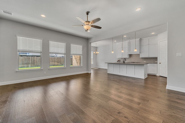 unfurnished living room featuring ceiling fan with notable chandelier, dark hardwood / wood-style flooring, plenty of natural light, and sink