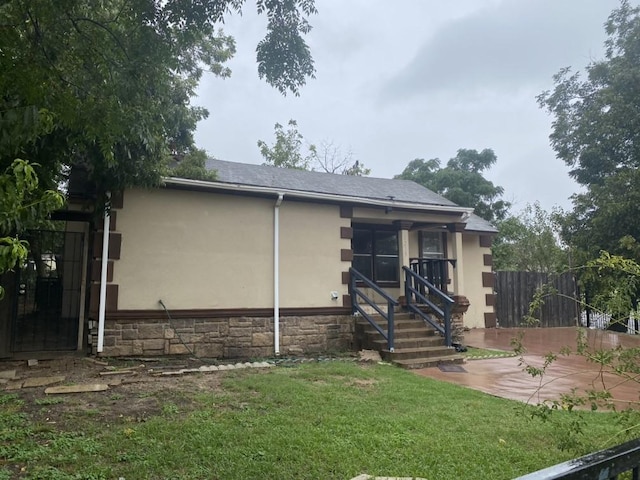 view of front of home with a front lawn, fence, stucco siding, a patio area, and stone siding