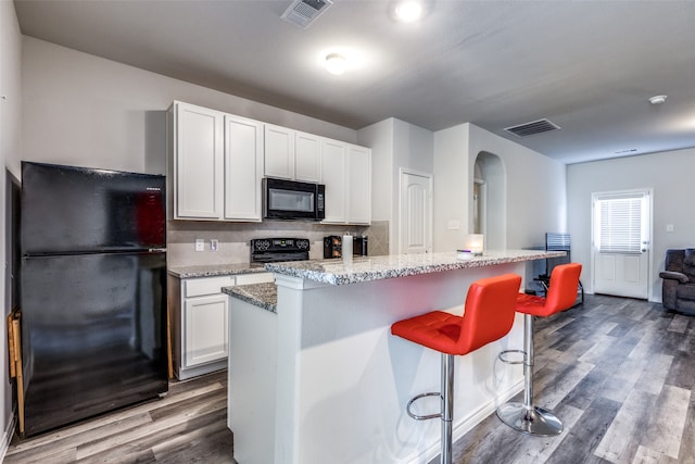 kitchen with light stone counters, white cabinetry, black appliances, dark hardwood / wood-style floors, and a kitchen island