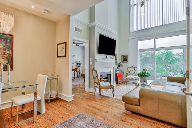 living room featuring a towering ceiling, ceiling fan, a fireplace, and light hardwood / wood-style flooring