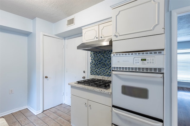 kitchen with a textured ceiling, oven, stainless steel gas stovetop, white cabinets, and light hardwood / wood-style floors