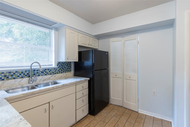 kitchen featuring white cabinets, backsplash, light wood-type flooring, sink, and black fridge