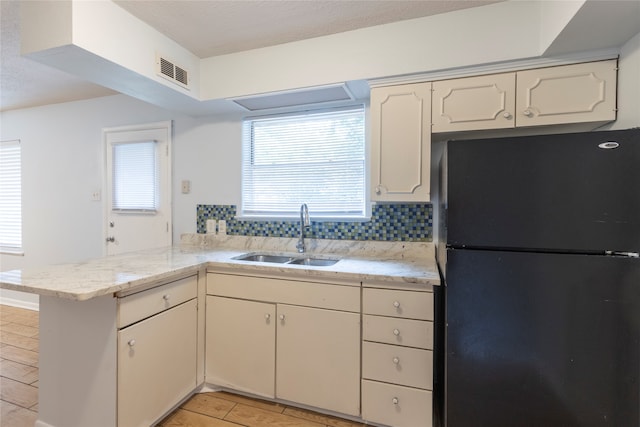 kitchen with black refrigerator, kitchen peninsula, sink, and backsplash