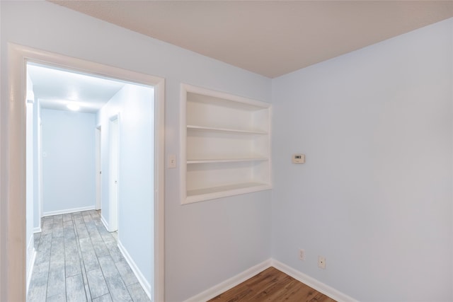 hallway with built in shelves and wood-type flooring