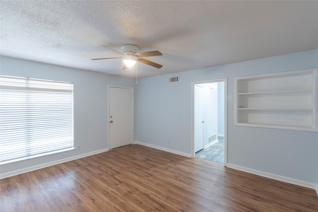 empty room with a textured ceiling, hardwood / wood-style floors, built in shelves, and ceiling fan