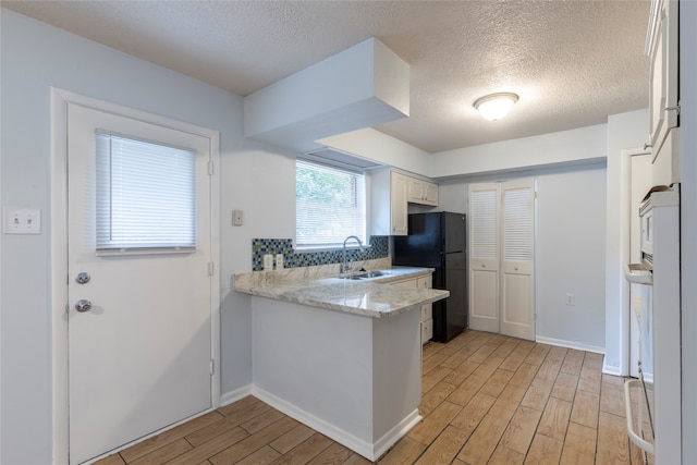 kitchen featuring light hardwood / wood-style floors, white cabinetry, sink, black refrigerator, and a textured ceiling