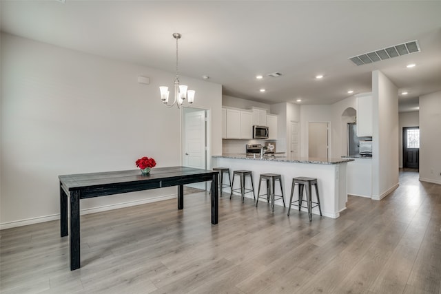 kitchen featuring light stone countertops, light hardwood / wood-style floors, kitchen peninsula, stainless steel appliances, and white cabinetry