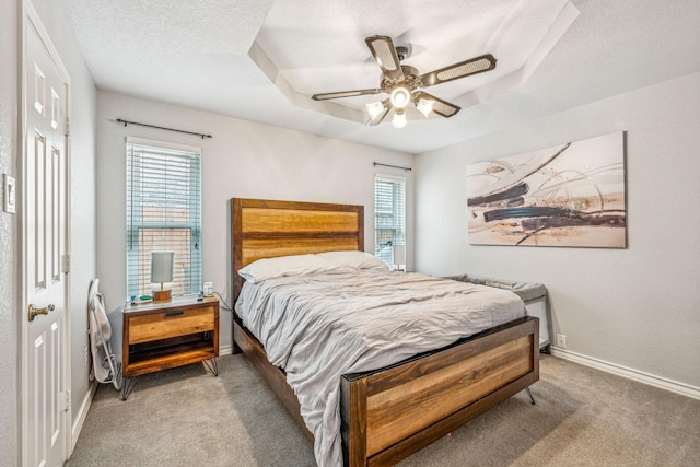 carpeted bedroom with multiple windows, ceiling fan, a tray ceiling, and a textured ceiling