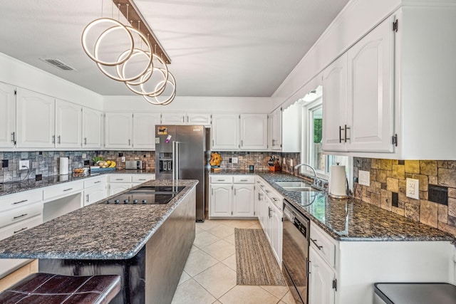 kitchen with dark stone countertops, appliances with stainless steel finishes, white cabinetry, sink, and a kitchen island