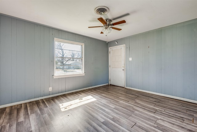 spare room with a ceiling fan, visible vents, baseboards, and wood finished floors