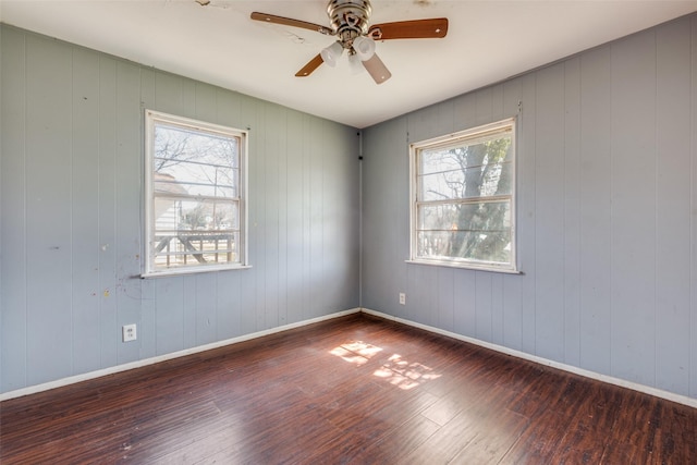 empty room with a ceiling fan, wood-type flooring, plenty of natural light, and baseboards