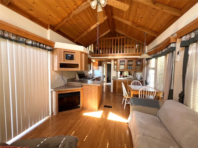 kitchen featuring stainless steel stove, hardwood / wood-style floors, kitchen peninsula, ceiling fan, and vaulted ceiling with beams