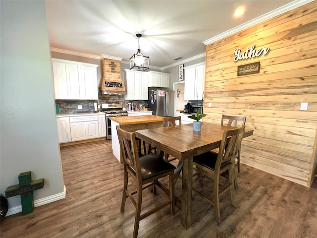 dining area with crown molding, dark wood-type flooring, and wooden walls