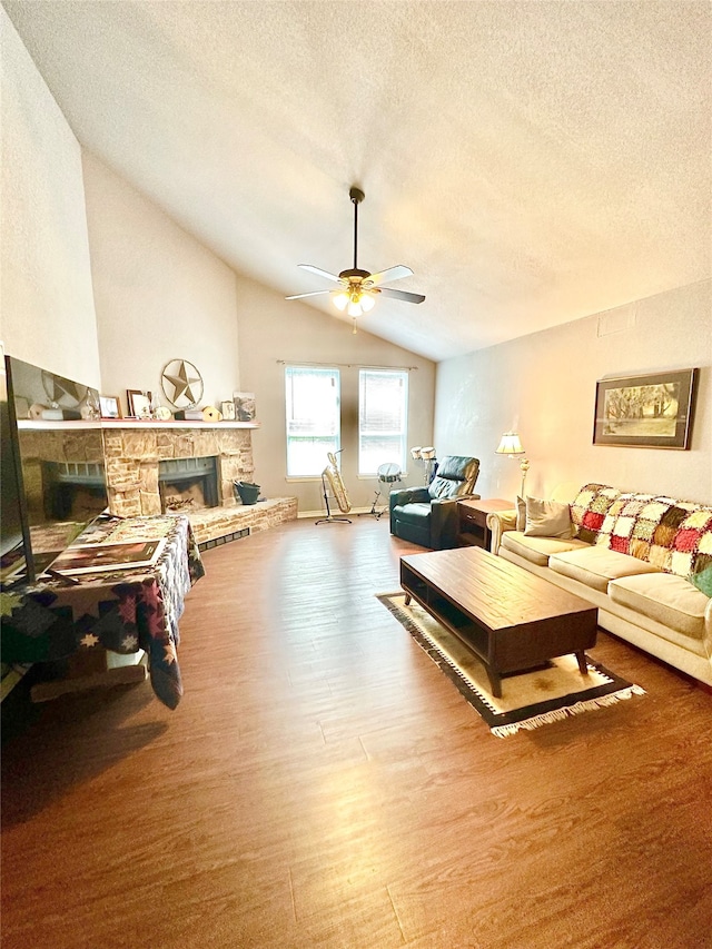 living room with vaulted ceiling, hardwood / wood-style floors, a stone fireplace, ceiling fan, and a textured ceiling