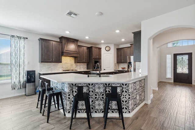 kitchen with a kitchen bar, a healthy amount of sunlight, sink, and premium range hood